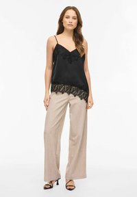 Črna satenska majica na naramnice z čipkastim robom na spodnjem delu, kombinirana s širokimi bež hlačami in črnimi sandali z naramnicami. Gladek rob in nežni poudarki.