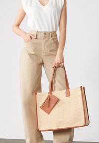 Beige kootud ostukott tan värvi nahkristide ja ääristega. Includeerib sobiva nahast kaarditasku, millel on tuti detail.