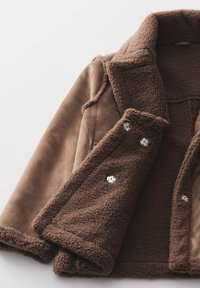 Bordeaux suède jack met een zachte, gewatteerde fleece voering. Heeft een brede kraag en drie decoratieve knopen aan de voorkant.