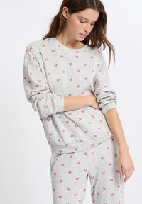 Sudadera gris claro con patrones de corazones rojos, cuello redondo y corte relajado. Tejido suave con puños y dobladillo acanalados.