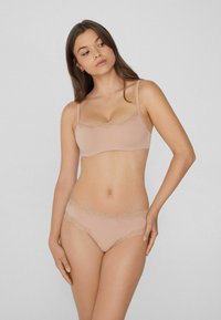 Sada podprsenky a kalhotek v měkké béžové tkanině s krajkovým lemem. Podprsenka má nastavitelná ramínka a bezšvový design, zatímco kalhotky mají vroubkovaný krajkový okraj.