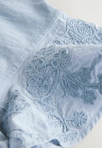 Tissu bleu clair avec broderie florale détaillée et coutures texturées dans divers motifs de fleurs et de feuilles.