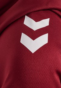 Close-up of maroon textured fabric with two white downward-pointing chevron shapes printed on it.