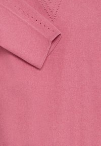 Manche de pull rose tricoté pliée sur le corps avec de petits trous décoratifs près du poignet et de la zone en V du col.