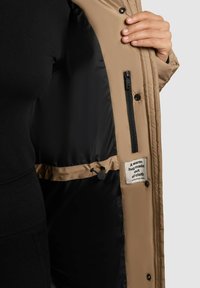 Karmiinpunane vooderdatud jakk musta voodriga, millel on lukk-tasku, reguleeritav nöör ja kangasilt tekstiga.