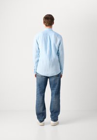 Camicia azzurra a maniche lunghe con colletto a bottoni, tessuto testurizzato, abbinata a jeans blu larghi e sneakers bianche.