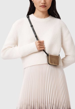 Maglione crema con polsini a coste, abbinato a una gonna plissettata rosa chiaro. Un piccolo borsellino in pelle dorata pende da una tracolla nera.