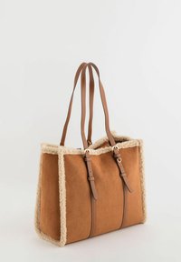 Sac fourre-tout en daim marron avec garniture en peau retournée beige, deux anses en cuir marron et accents métalliques dorés. Forme rectangulaire.