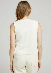 Haut sans manches de couleur crème en tricot texturé. Il présente un col montant et un design droit et simple. Vue de dos.