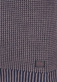 Stickad tröja i mörklila och ljusgrå med ribbad textur. Har en vävd logotyp-lapp i det nedre hörnet.