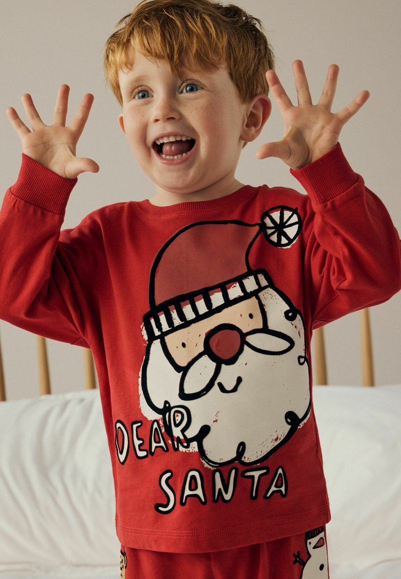 Set de pijamale din bumbac roșu cu un print mare cu Moș Crăciun și textul "DRAGĂ MOȘ CRĂCIUN". Mâneci lungi, decolteu rotund, design jucăuș.