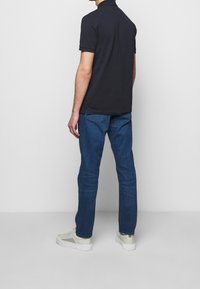 Polo bleu marine et jean bleu. Le polo a des manches courtes et un col, tandis que le jean est droit avec des coutures visibles. Baskets blanches.