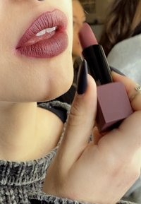 Matte mauve lipstick in a sleek black tube with a square base. Close-up of lips with a smooth texture and natural shine underneath.