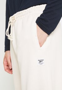 Krämfärgade bomulls-joggare med elastiskt midjeband och snörning. Har sidofickor och en Reebok-logotyp för varumärkesidentifikation.