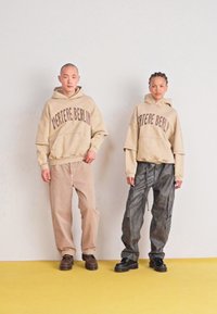 Felpe oversize beige con il testo "Vertere Berlin", abbinate a pantaloni beige chiaro e pantaloni cargo scuri e texturizzati. Calzature nere.