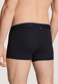 Zwarte boxershorts gemaakt van zachte stof, met verticale strepen, een effen zwarte tailleband met "CALIDA" in reliëf, en een boxy snit.