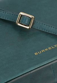 Borsa a tracolla in pelle verde acqua con forma rettangolare, dotata di una fibbia quadrata in metallo dorato e logo "BURKELY" in rilievo dorato. Texture liscia.