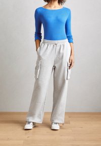 Blue ribbed long-sleeve top paired with gray elastic-waist sweatpants featuring side pockets and a loose fit. Sneakers complete the outfit.