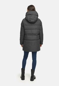 Black padded coat with a hood, featuring a quilted design and a slightly longer back. Paired with dark jeans and black ankle boots.