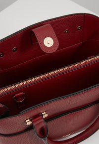 Rote Lederhandtasche mit genarbter Struktur, goldfarbenen Beschlägen, Reißverschlussfach und Innentaschen. Verfügt über einen magnetischen Verschluss.