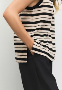 Black and beige striped sleeveless top with a round neckline, side slits, and a relaxed fit, paired with black pants.