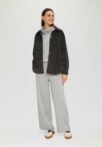 Zwarte corduroy knoopovershirt, grijze coltrui, grijze wijde broek en tan sneakers met zwarte accenten. Gladde textuur en ontspannen pasvorm.