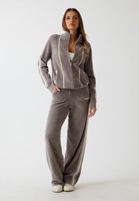 Szara welurowa kurtka zapinana na zamek z białymi pasek i dopasowane spodnie z bocznymi paskami. Oba elementy mają luźny krój i miękką teksturę.