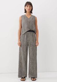 Zwart-wit geblokte mouwloze top met een V-hals, gecombineerd met hoge wijde broek. Glad, lichtgewicht materiaal. Platte sandalen.