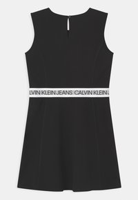 Czarna sukienka bez rękawów, z białym elastycznym pasem oznaczonym "CALVIN KLEIN JEANS" oraz detalem w kształcie dziurki na plecach.