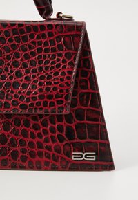 Borsa in pelle goffrata rossa e nera con forma triangolare, pattina magnetica e dettaglio del logo in argento sul fronte.