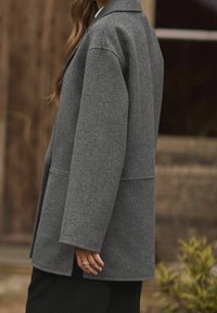 Manteau gris en mélange de laine, coupe décontractée, manches longues et col à revers. Comprend des poches avant et un design légèrement oversize.