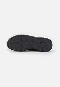 Suela de zapato deportivo negro con goma texturizada para un mejor agarre, que presenta un diseño de banda de rodadura con patrón y un detalle de logo embosado en la superficie.