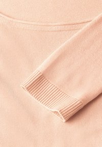 Hellrosa Pulloverstoff mit glatter Textur, ausgestattet mit einem gerippten Bündchen und einem abgerundeten Ausschnitt, der durchgehende Nähdetails aufweist.