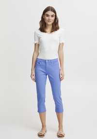 Bílý top s krátkým rukávem a krajkovým lemem, kombinovaný s světle modrými zkrácenými kalhotami a béžovými šlapkami. Jednoduchý, přiléhavý design.