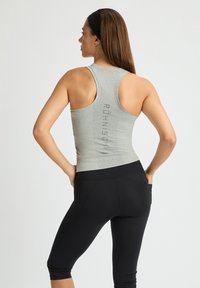 Camiseta sin mangas gris con un diseño de espalda nadadora, presenta un patrón texturizado y un logo impreso en la parte trasera. Combinada con unos leggings capri negros.