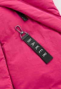 Spilgti rozā audums ar strukturētu apdari, ar melnu birku ar uzrakstu "BAKER" un metāla klipša stiprinājumu.
