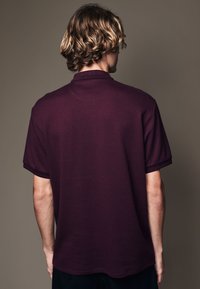 Polo-shirt bordeaux à manches courtes avec un motif texturé et un col classique, présentant une coupe décontractée et des détails de couture visibles.