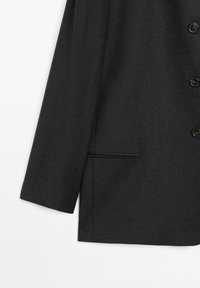 Black wool-blend blazer with a structured design, single chest pocket, and round black buttons, featuring a smooth matte texture.
