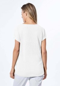 Witte, korte mouwen top met een relaxed fit, zachte textuur, ronde zoom en een brede halslijn. Achteraanzicht toont een naadloos ontwerp en eenvoudige styling.