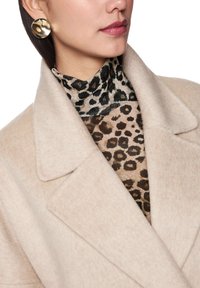 Beige wool coat with a wide collar, layered over a brown and black leopard print turtleneck. Gold circular earrings add a metallic accent.