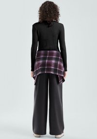 Czarny prążkowany top z długim rękawem połączony z fioletowo-czarną koszulą w kratę, zawiązaną w pasie, noszony na luźnych czarnych spodniach i jasnych butach.