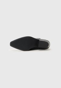 Suela de zapato negra con forma puntiaguda, agarre de goma texturizada y un acento gris suave cerca del talón. Diseño limpio y minimalista sin adornos.