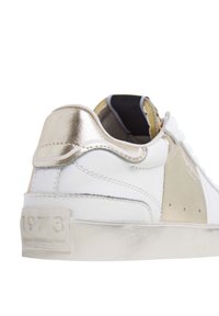 Sneaker bianca con accenti metallici dorati. Presenta pelle liscia, un tallone testurizzato e un dettaglio embossato "1973" sulla linguetta del tallone.