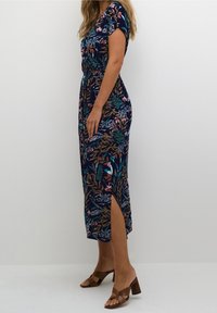 Robe maxi florale bleu marine avec une taille cintrée, des manches courtes et une fente latérale. Le tissu présente une texture lisse avec des motifs de plantes colorées.