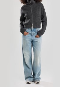Suéter gris corto con cuello alto, combinado con jeans de pierna ancha en azul claro y zapatillas grises. Tejido de punto texturizado en el suéter.