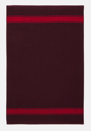 Toalha bordô com uma textura suave, apresentando duas faixas vermelhas ousadas na parte superior. Forma retangular, adequada para uso em banheiro.