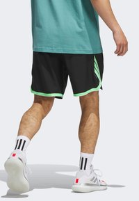 Svarta sportshorts med neongröna detaljer, som har en meshstruktur, sidostänger och en lös passform, tillsammans med vita strumpor och sneakers.