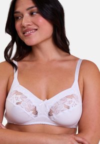 Soutien-gorge blanc avec détails en dentelle. Tissu doux, bretelles réglables, bordures festonnées et un petit nœud au centre. Bonnets lisses et arrondis.