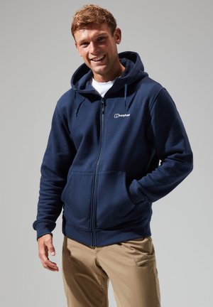 Navy zip-up hoodie made of fleece material with a kangaroo pocket, adjustable drawstring hood, and white logo on the chest.