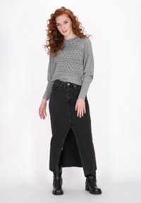 Grijze gebreide trui met een textuurpatroon en geribde manchetten, gecombineerd met een zwarte denim maxirok met een voorzicht en enkellaarzen.
